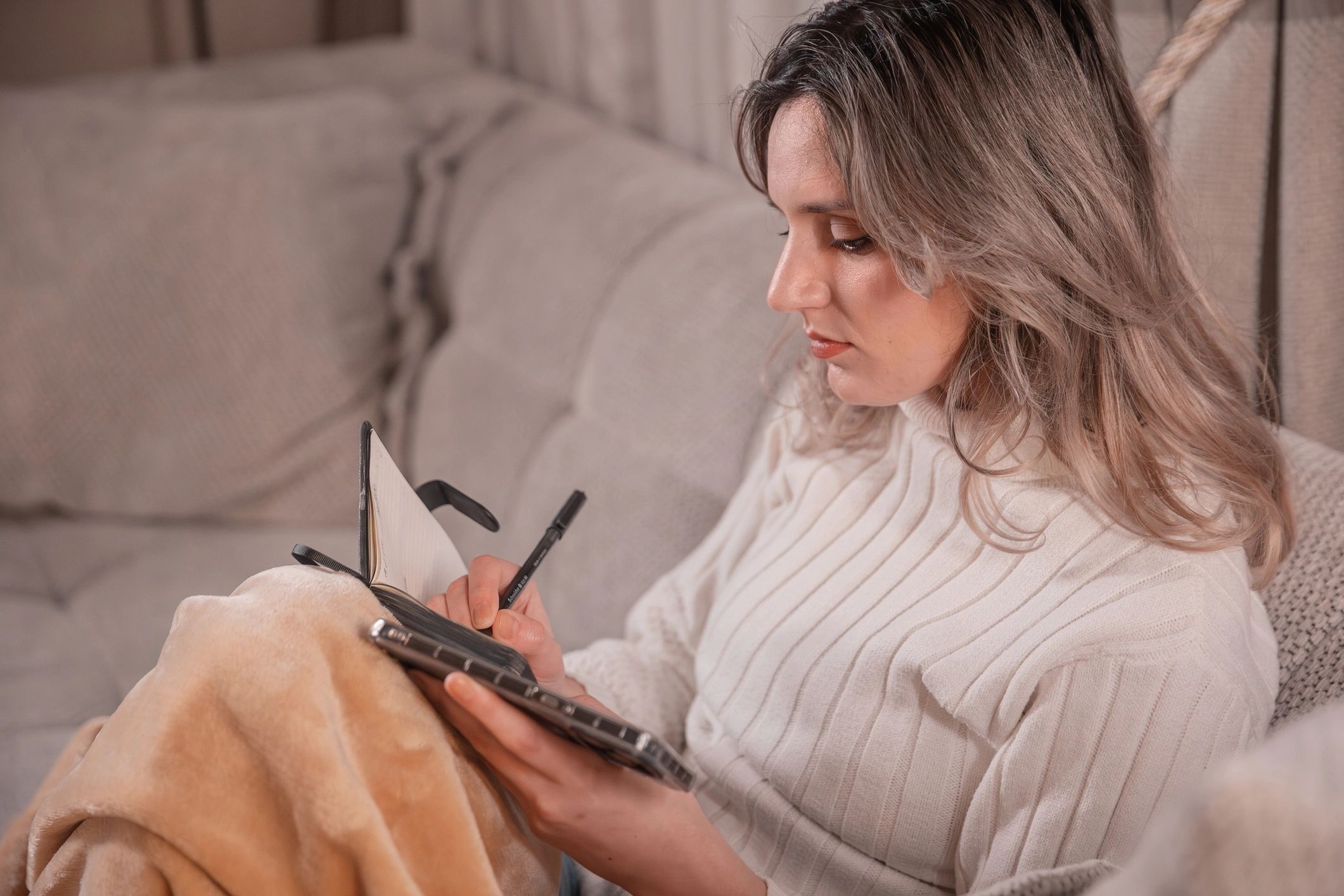 Persona escribiendo en un diario desde el sofá